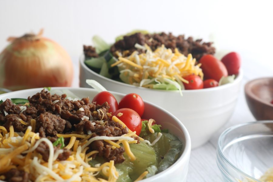 Healthy lo-carb burger bowl featuring seasoned ground beef, crisp lettuce, shredded cheese, cherry tomatoes, dill pickles and onions